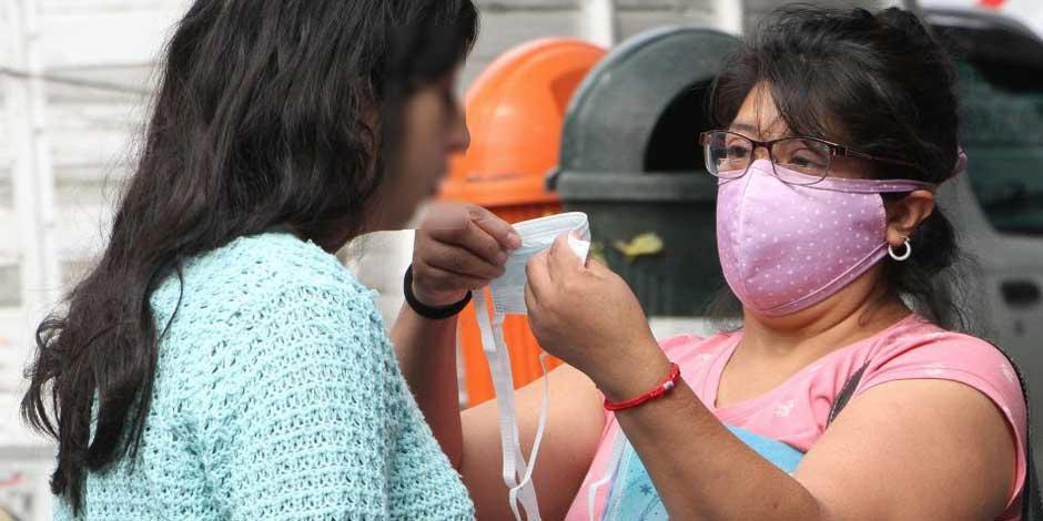 Una mujer ayuda a una joven a colocarse el cubrebocas para no contagiarse con COVID-19