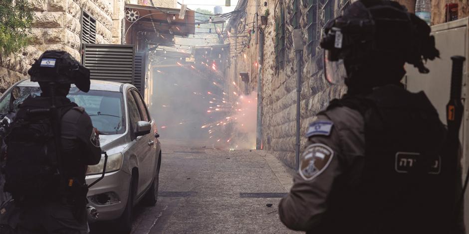 Policía fronteriza israelí aguarda mientras manifestantes palestinos disparan fuegos artificiales hacia ellos, ayer.