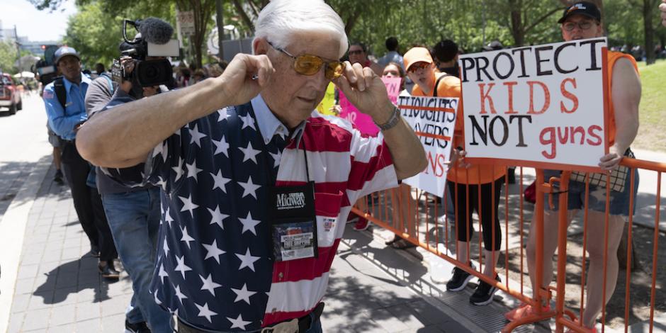 Un miembro de la Asociación Nacional del Rifle se tapa los oídos mientras pasa junto a los manifestantes durante la reunión anual de la NRA, en Houston.
