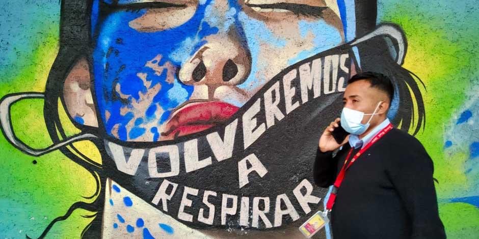 COVID-19: Un hombre con cubrebocas camina frente a un mural con la leyende "Volveremos a respirar"