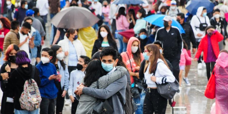 Una pareja se abraza mientras esperan cruzar la avenida; al fondo, decenas de personas se protegen de la lluvia en calles de la CDMX.