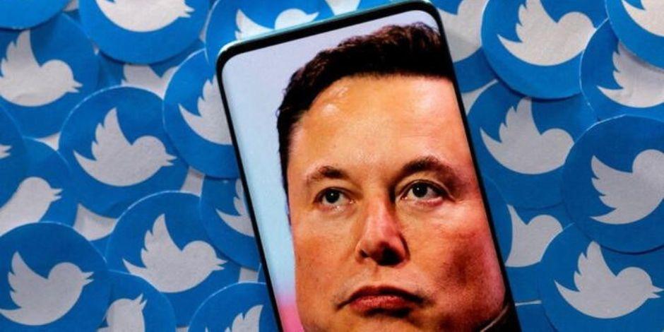 Elon Musk en un teléfono inteligente colocado en los logotipos impresos de Twitter.