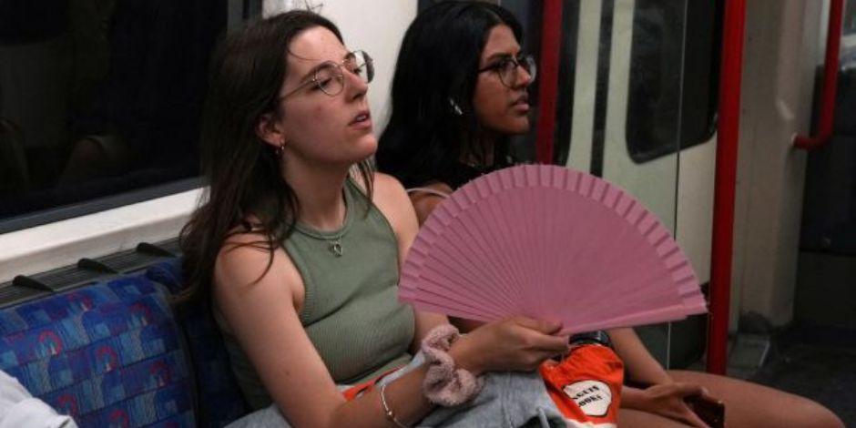 Una mujer se refresca con un abanico al interior de un vagón del metro de Londres.