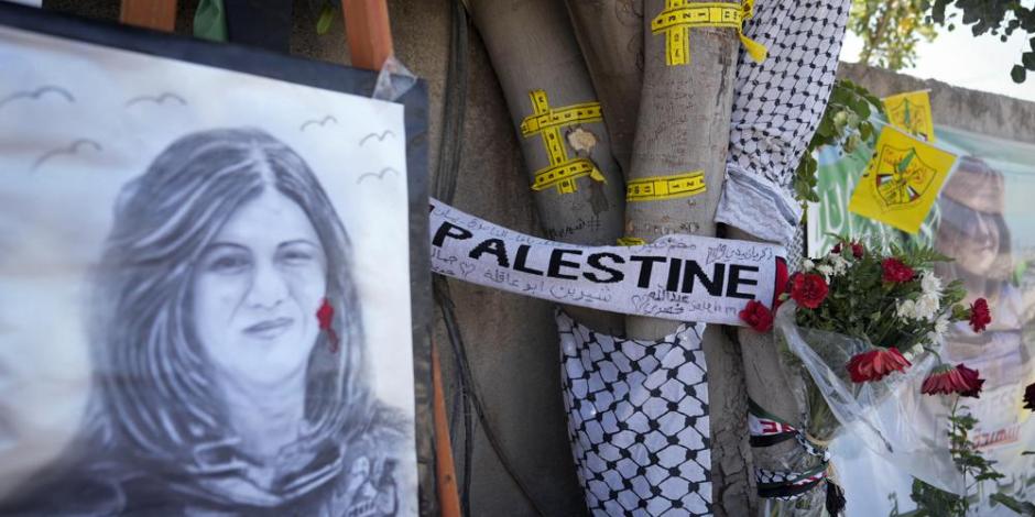 La cinta amarilla marca los agujeros de bala en un árbol y un retrato y flores crean un monumento improvisado, en el lugar donde la periodista palestina Abu Akleh fue asesinada a tiros.