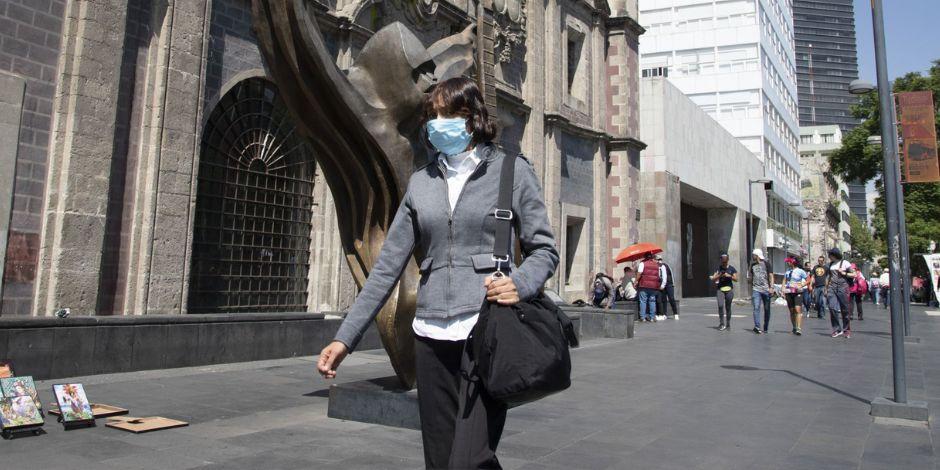 Una mujer camina por la calle con un cubrebocas para protegerse de enfermedades respiratorias