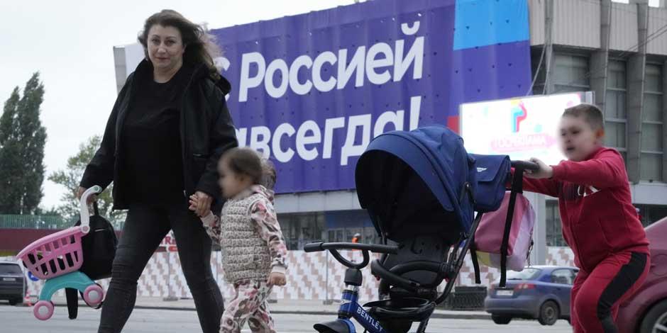 Una mujer y sus hijos cruzan una calle, con un enorme cartel de fondo que dice "¡Rusia para siempre!", en Lugansk, Ucrania, el 28 de septiembre de 2022