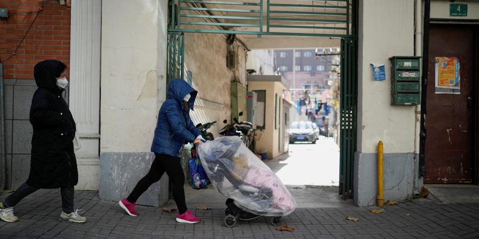 Una mujer con una máscara facial empuja una carriola cubierta de plástico con un bebé adentro, mientras continúan los brotes de la enfermedad por coronavirus (COVID-19) en Shanghái, China, el 18 de diciembre de 2022.