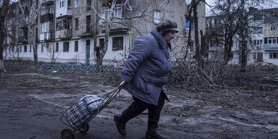 Una mujer camina a un centro de distribución de ayuda humanitaria frente a una vivienda dañada por los ataques rusos en Kupiansk, en la región de Járkiv, Ucrania, el miércoles 26 de diciembre de 2022.