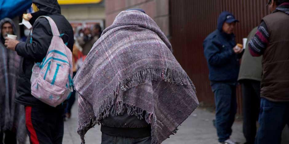 Una persona camina por la calle con una cobija a cuestas para protegerse de las bajas temperaturas