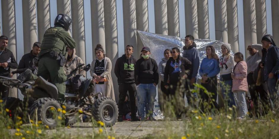 Un agente de EU habla con migrantes que cruzaron la frontera para pedir asilo, ayer.