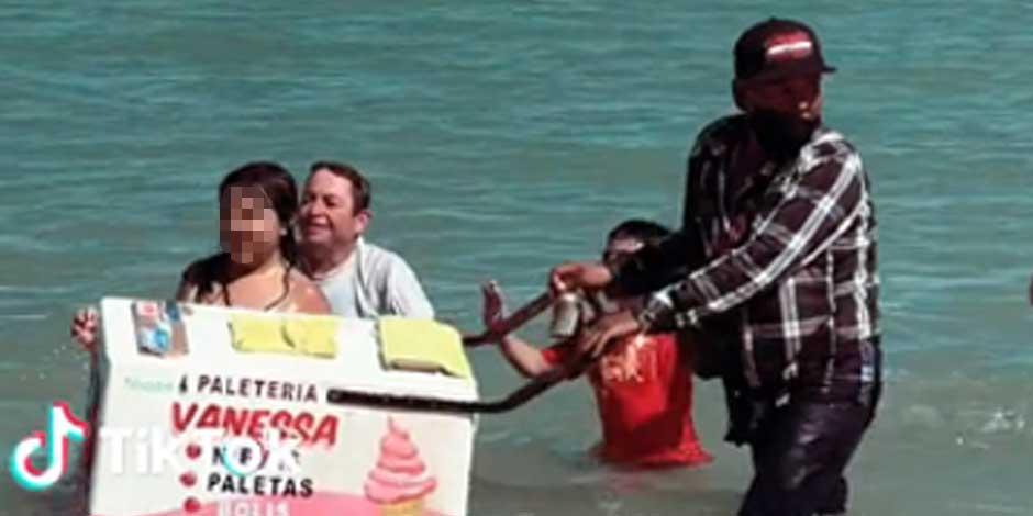Vendedor de paletas y helados lleva su carrito entre las olas del mar