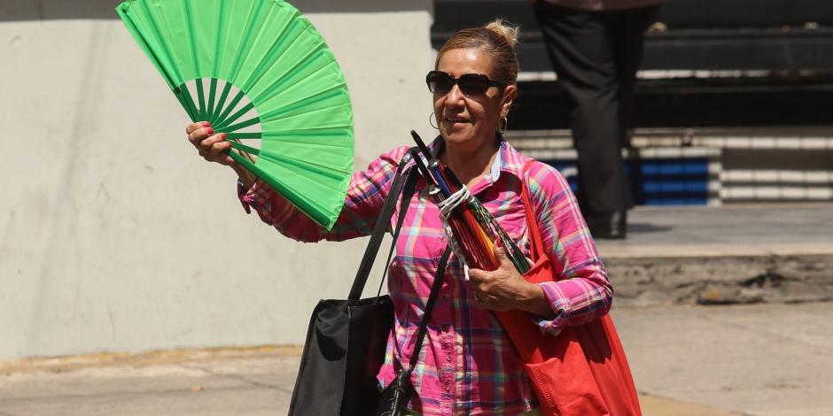 Una mujer se refresca con un abanico mientras camina por Paseo de la Reforma