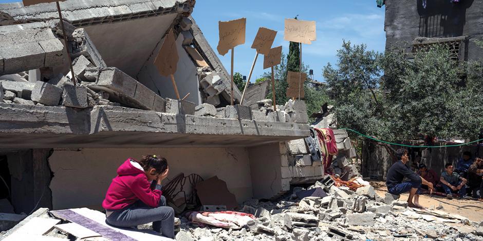 Ciudadanos se sientan frente a inmuebles golpeados en la última semana en Gaza, ayer.