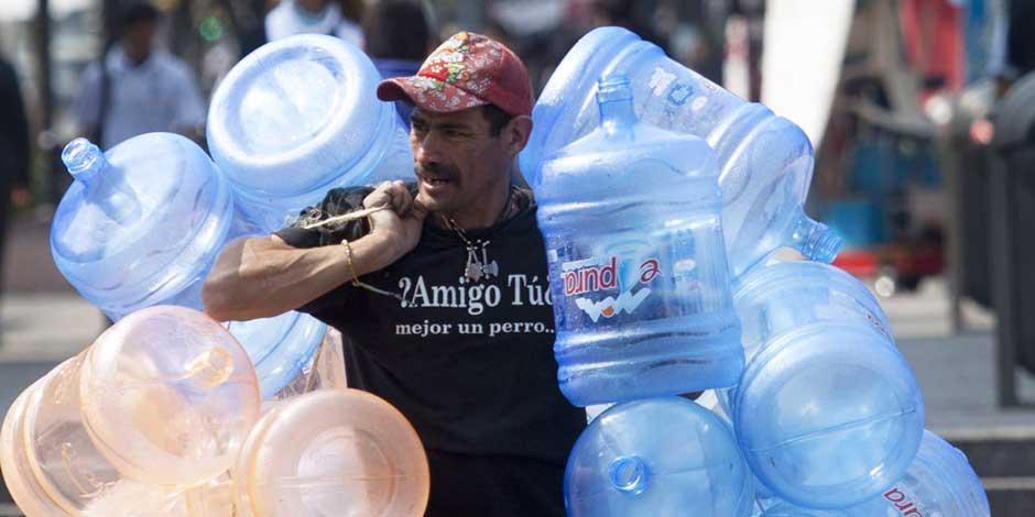 En la imagen, un hombre carga varios garrafones de agua en la calle