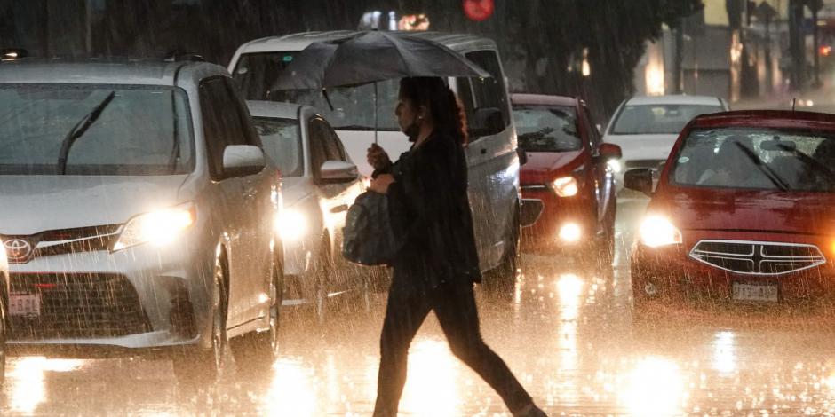 Una mujer con paraguas camina bajo la lluvia en calles de la CDMX.