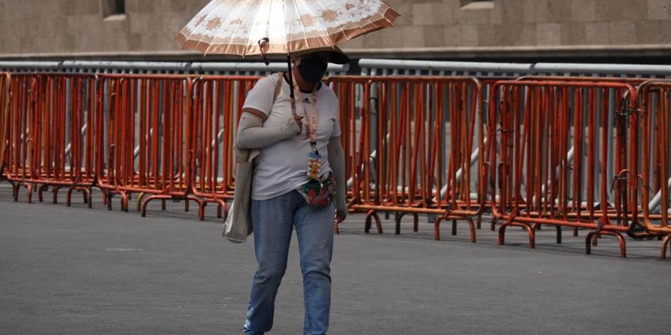 Tercera ola de calor continúa en México; en foto, una mujer se cubre del sol mientras camina por el Zócalo de la Ciudad de México.