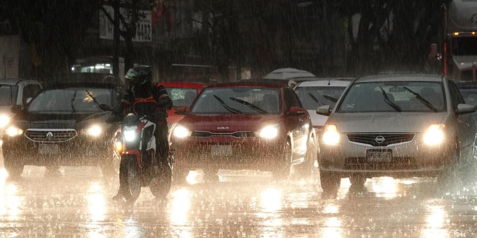 Un motociclista al frente de varios autos espera la luz verde para continuar su camino, en una tarde de lluvia en la CDMX