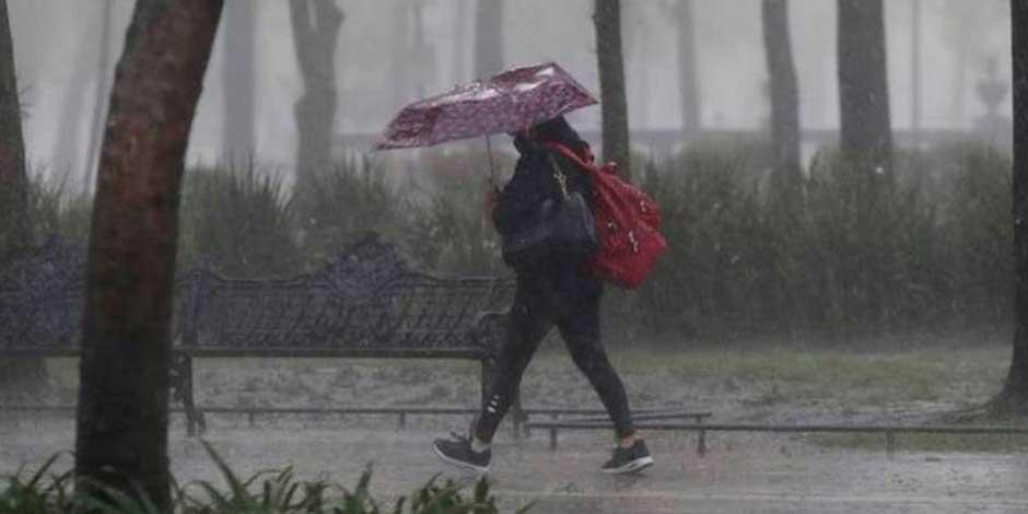Una mujer camina por la calle, tapándose con un paraguas de la lluvia