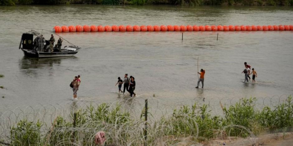 Migrantes cruzan el Río Grande desde México; pasan por la barrera de boyas puesta por las autoridades en el río, en Texas.