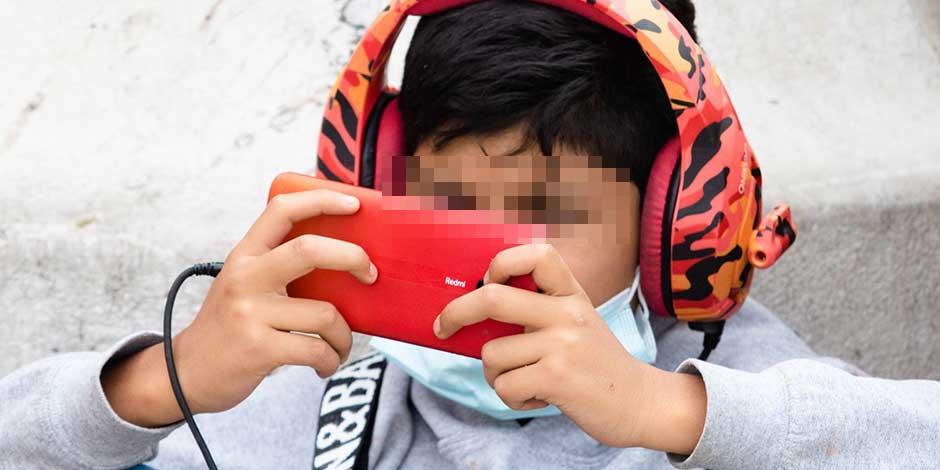 Un niño con audífonos se entretiene con un videojuego en un celular