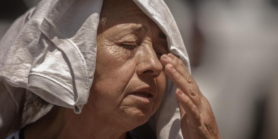 Una mujer de la tercera edad cubre su cabeza y seca su sudor ante el fuerte calor