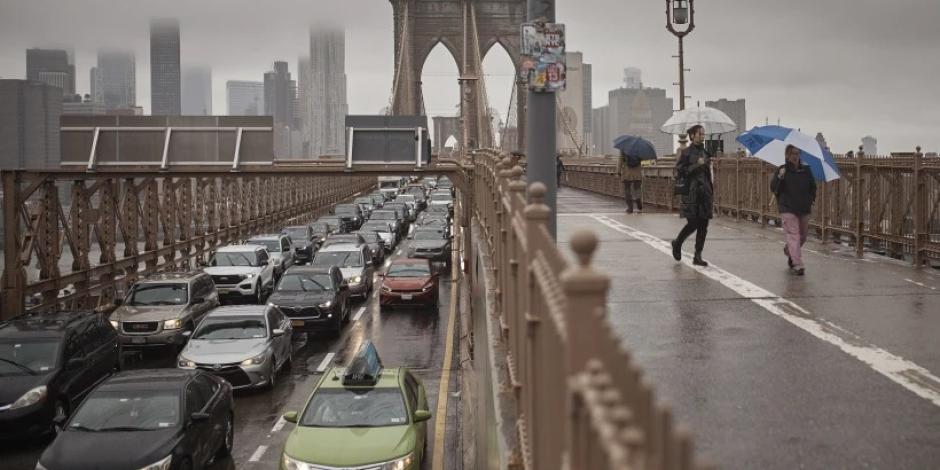 Personas con sombrillas caminan a un costado de los vehículos por el Puente de Brooklyn, luego de las fuertes lluvias del viernes 29 de septiembre de 2023, en Nueva York.