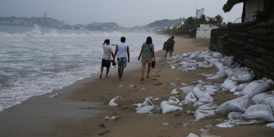 Un grupo de personas camina sobre una playa de Acapulco, horas antes de la llegada del huracán 'Otis'.