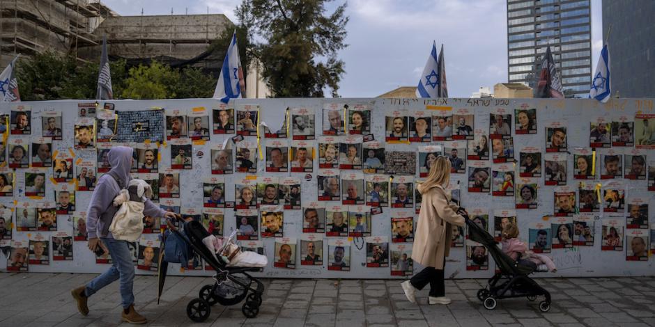 Ciudadanos caminan frente a vallas en Tel Aviv con pancartas de los rostros de las víctimas que secuestró Hamas, ayer.