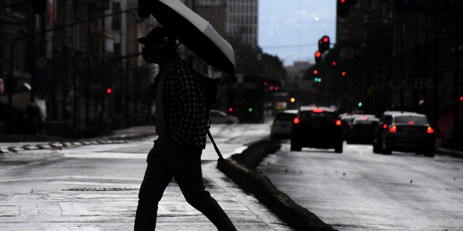Un hombre cruza la calle mientras usa un paraguas para protegerse de la lluvia.