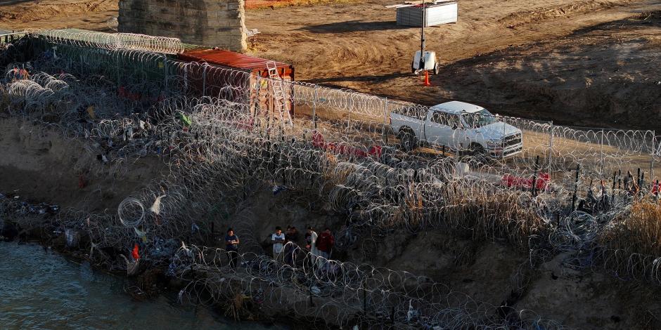 Migrantes observan la valla de alambre de púas a orillas del río Grande.