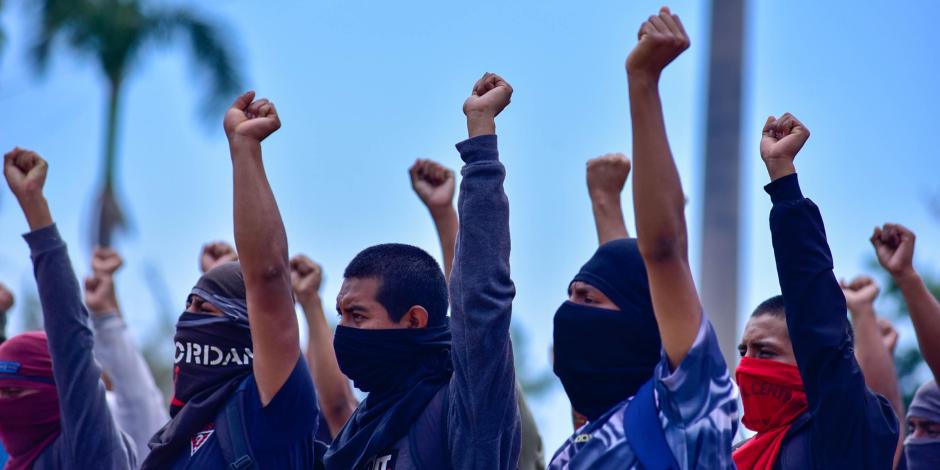 Estudiantes normalistas levantan el puño izquierdo durante una protesta para exigir justicia para Yanqui Kothan.