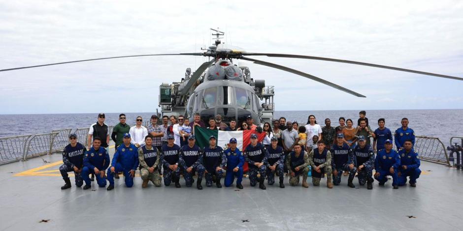 Los connacionales rescatados y personal de la Semar posan frente al helicóptero que los trasladó al buque Holbox.