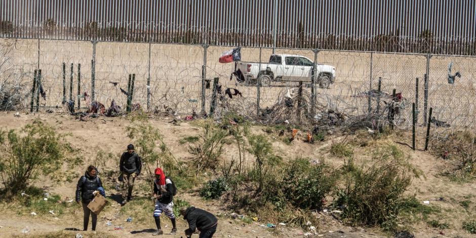 Un grupo de migrantes se paran en la zona fronteriza de Texas, mientras la GN de ese estado pasa detrás de ellos, ayer.