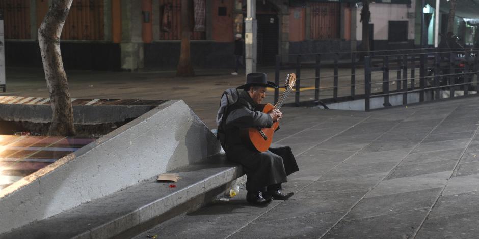 Un hombre toca su guitarra en una banca, en 2020.