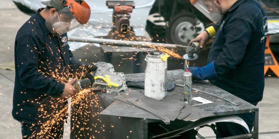 Dos trabajadores sueldan una pieza de autoparte.