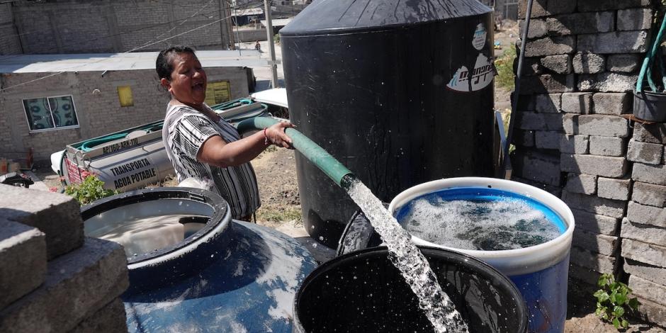 Una mujer llena tinacos con la manguera de una pipa.