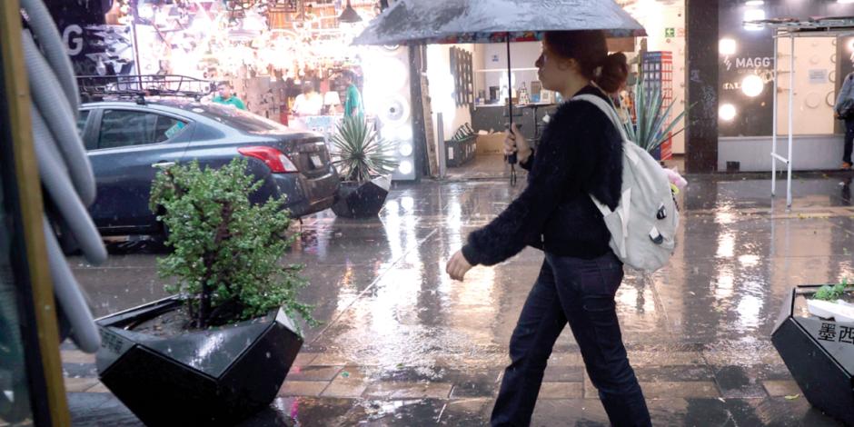 Una mujer se cubre de la lluvia con un paraguas, mientras camina por las calles de la Ciudad de México.