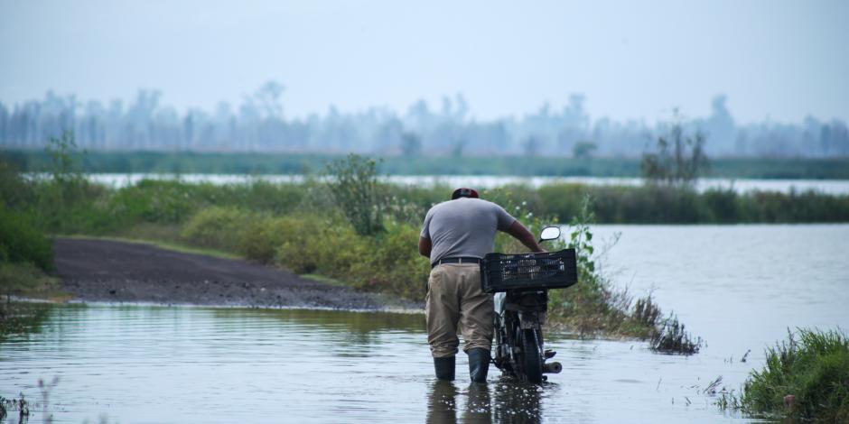 Un hombre arrastra su bicicleta entre un charco por las lluvias recientes.